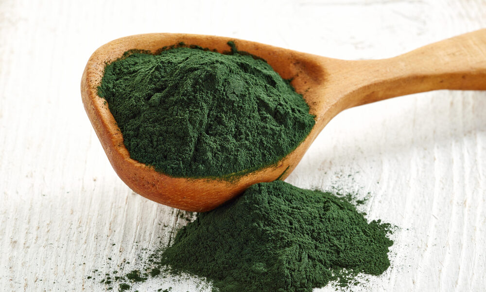 Spirulina para que sirve en polvo color verde oscuro en una cuchara de madera con fondo blanco