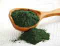 Spirulina para que sirve en polvo color verde oscuro en una cuchara de madera con fondo blanco