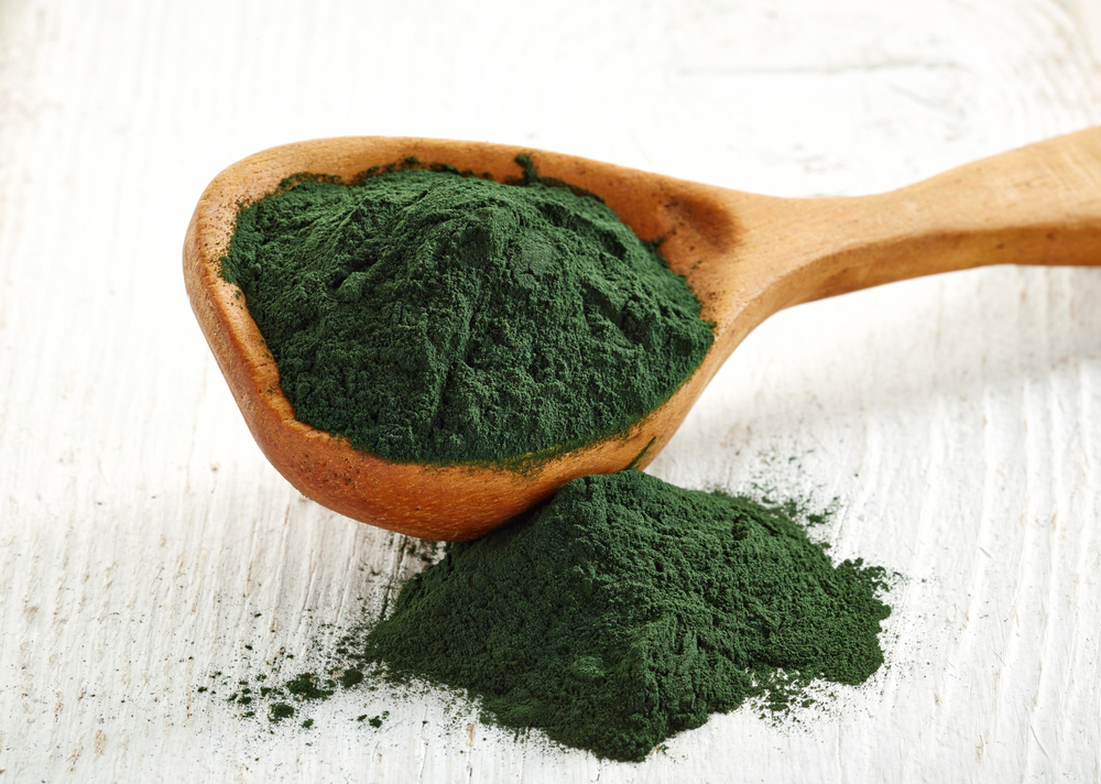 Spirulina para que sirve en polvo color verde oscuro en una cuchara de madera con fondo blanco